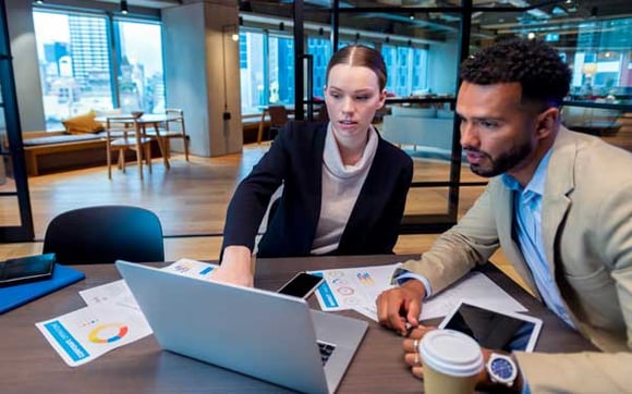 two coworkers looking at stats on a laptop