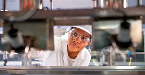 employee in safety glasses and hardhat inspecting manufactured items