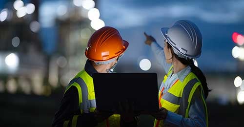 two people in hard hats looking at a screen on-site at night